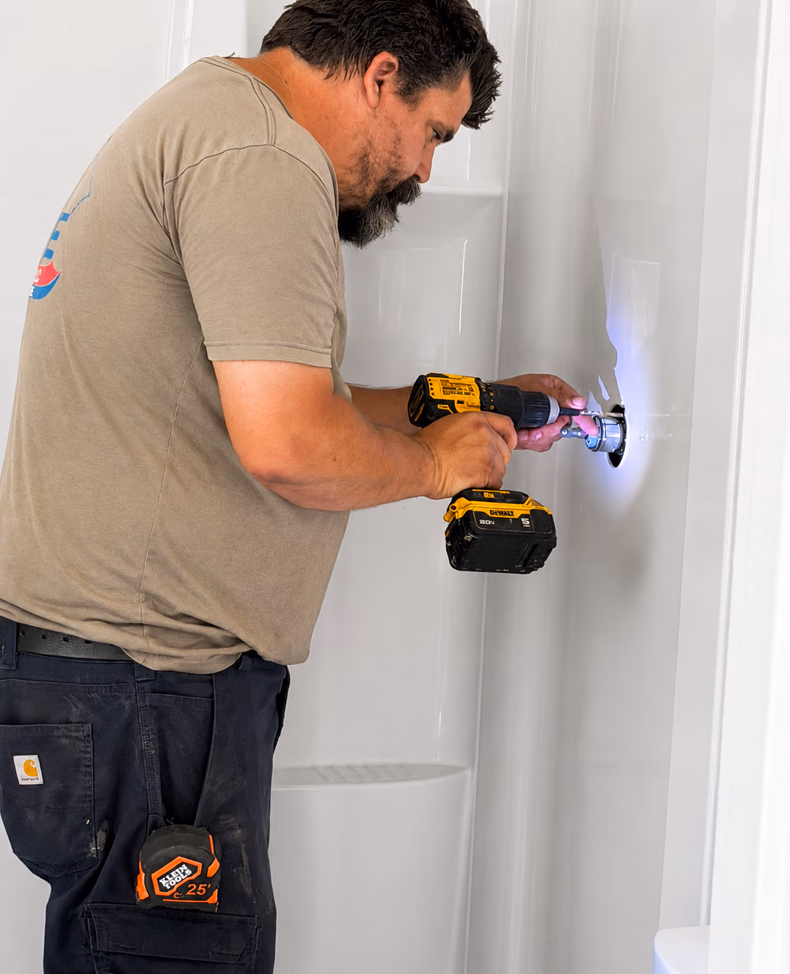 Man using a cordless drill to install plumbing inside a white shower stall.
