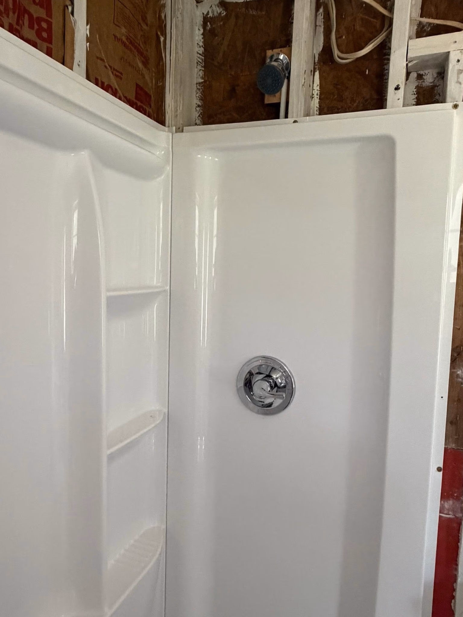 Partially installed white shower with built-in shelves and exposed wall insulation above.